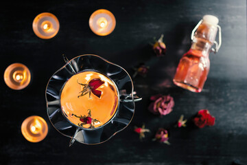 Top view of glassy round aroma oil lamp with glass essential oil bottle and dry flower rose flowers on a black table...