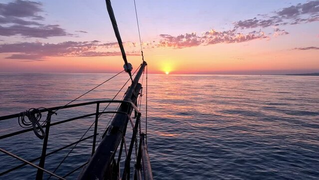 A sailing pirate yacht glides across the sea waves towards the setting sun. View on the sunset from the bow of the ship. Slow motion.