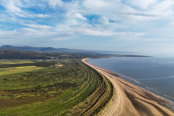Aerial view of a curved sandy beach against a blue sky and deep blue sea shore coastline