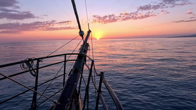 A sailing pirate yacht glides across the sea waves towards the setting sun. View on the sunset from the bow of the ship. Slow motion.