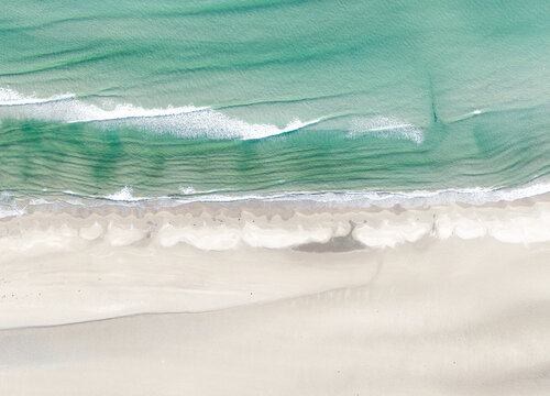 Aeriel birdseye shot of a shoreline in Wales, UK, turqoise sea waves lapping at a sandy beach 