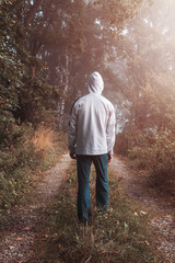 Young man in white hoodie and pants walking through misty fog forest from back - 646460483