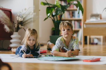 Siblings lying on stomach and painting at home with watercolors, markers and tempera paints, creating a model of planet Earth.