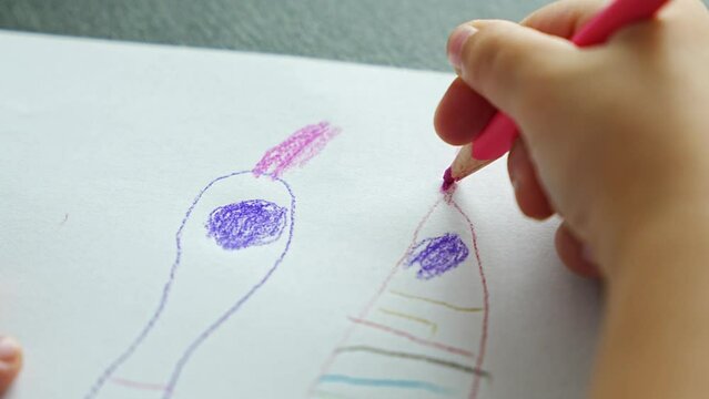 Close up view of hands of little girl draws with colored pencils in home. 