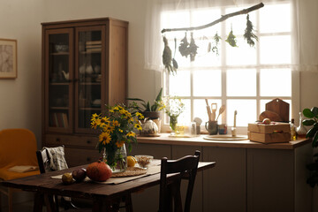 Bunch of yellow wildflowers in vase, ripe vegetables and other stuff on wooden table standing in...