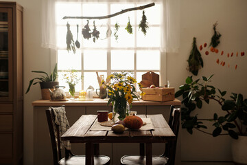 Fototapeta na wymiar Two wooden chairs standing by table with bunch of yellow garden flowers in vase, ripe pumpkin and eggplants and mug against kitchen counter