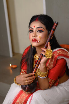 Portrait young Indian girl wearing traditional saree, gold jewellery, bangles holding a musical instrument Ektara in studio lighting indoor. Indian culture, religion and fashion