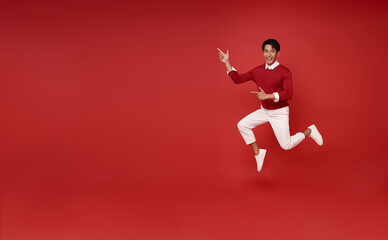 Fototapeta na wymiar Full length handsome happy smile asian man 20s jumping and hand pointing finger present something isolated on red copy space background.