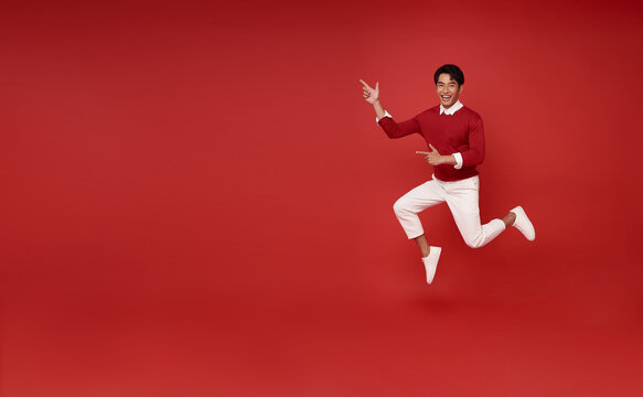 Full length handsome happy smile asian man 20s jumping and hand pointing finger present something isolated on red copy space background.