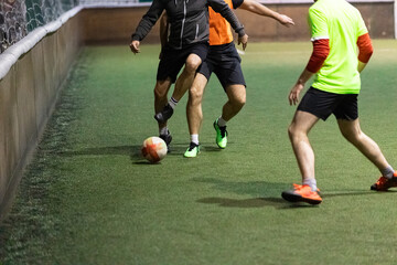 Football Futsal ball and man legs on artificial grass field indoors.
