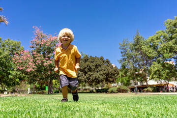 a little blond boy of three years old runs in the park on the green grass