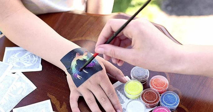 Kid's animator is creating a Shimmering sparkling glitter tattoo on a child's hand at a birthday party
