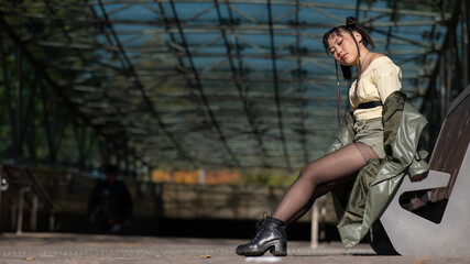 A young Asian woman sits on a bench at the subway exit. 