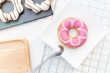 A beutiful pink donut on a white plate with a spoon. Doughnuts flat lay composition.