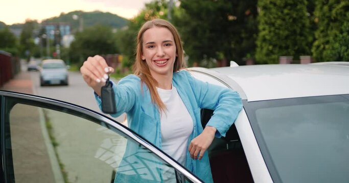 Portrait of young woman standing near car holds keys with delighted and show keys wants to buy new automobile in car. Attractive girl holding a key from her new car, smiling and singing.