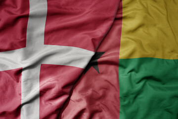 big waving national colorful flag of denmark and national flag of guinea bissau .