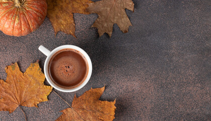 Cup of coffee next to autumn leaves and pumpkin on brown background, Top view