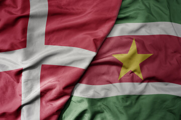 big waving national colorful flag of denmark and national flag of suriname .
