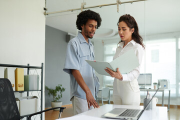 Coworkers discussing figures in annual report when standing in office