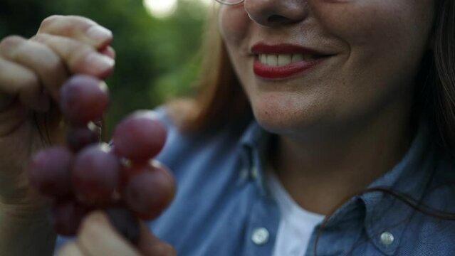 Portrait of smiling Caucasian woman eating sweet pink grape healthy food outdoors. Young woman eating grapes. People, food and drink, lifestyle concept.High quality FullHD footage