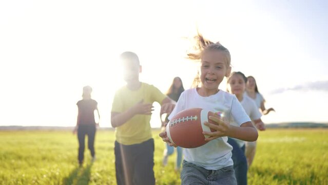 children playing rugby in the park. a group of children play american football run outdoors in the park in summer. happy family kid dream concept. family children play american lifestyle football run