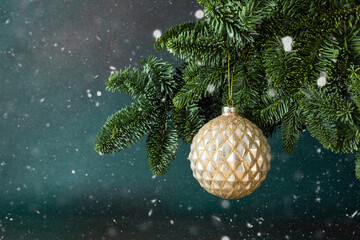 Golden Christmas ball hanging on a fir branch on a green background among the snow, Christmas background