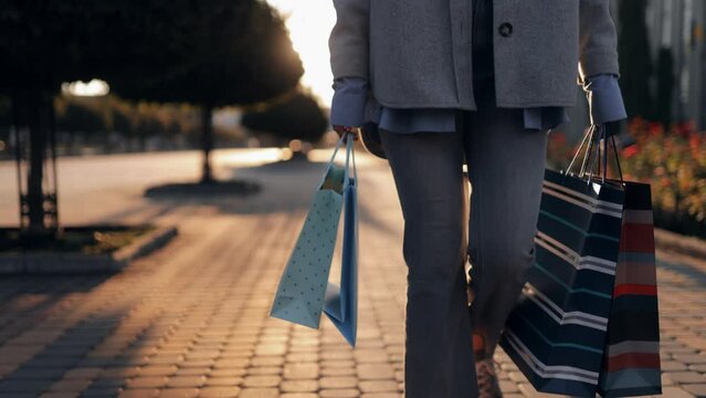A young girl in stylish clothes in jeans and with shopping bags in her hands walks down the city street, close-up. Slow motion, front view