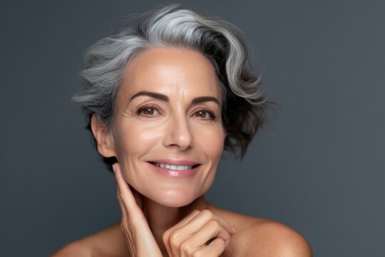 Portrait of a fifty year old European woman with happy well-groomed face on gray background. Rejuvenation concept.