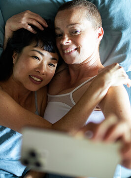 Happy young mixed lesbian couple taking a selfie with a smartphone in the bedroom