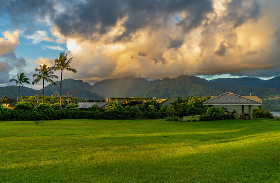 Sunrise illuminates storm clouds over Hanalei mountains with the plant covered buildings of 1 Hotel in the foreground