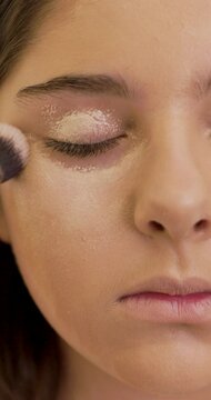 Close-up portrait of a girl model, make-up artist applies eye shadow primer or corrector with a make-up brush.