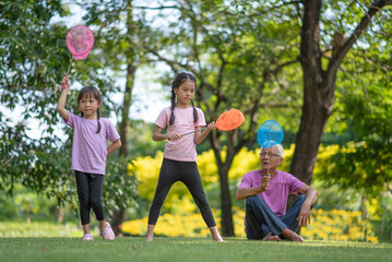 Happy Asian family children having fun and catches a net of insects with her grandfather in the park