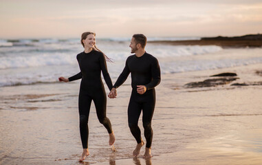 Happy surfers couple holding hands while running together on the beach