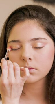 Portrait of a girl model at make-up artist who is applies eye shadow with a make-up brush to a her.