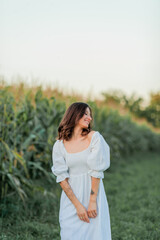 Fototapeta na wymiar Young beautiful woman 26 years old in white simple dress in summer field. Green corn. Summer. Rustic style.