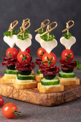 Canape with cheese, cherry tomatoes, sausage and black olives on wooden board