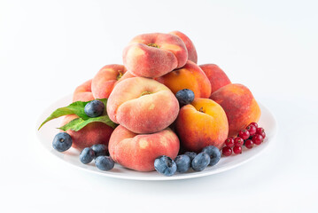 On a white background in a plate there are peaches, blueberries and red currants. Healthy food concept.