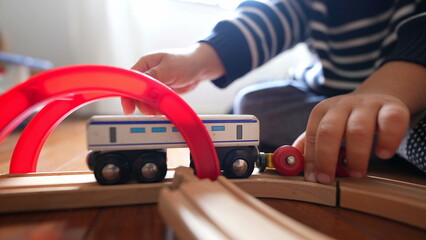Close-up child hand playing with traditional toys on wooden train tracks. Little boy pushes retro wagon
