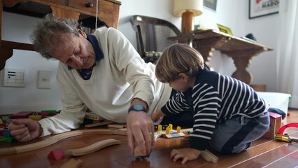 Elderly Man and Young Boy Building Train Set on Wooden Floor, grandfather and child grandson bonding time together