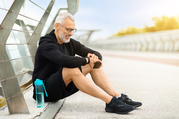 Senior sportsman sitting on the ground, checking his smart watch