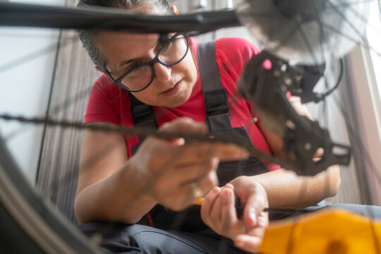Cute Caucasian female worker holding and repairing bicycle wheel in bicycle workshop.