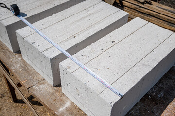 White aerated concrete blocks close-up. Measuring the size of a gas block with a tape measure. Construction of a house from aerated concrete blocks and bricks.