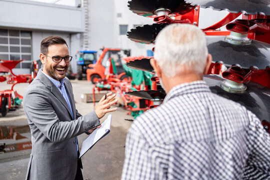 Sales manager selling harrow equipment to the farmer at dealership. Buying tractors and agricultural equipment.
