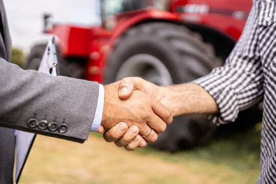 Buying new tractor agricultural machine. Close up view of buyer and dealer handshake at tractor dealership.