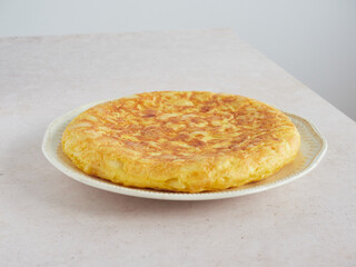 golden and appetizing whole homemade Spanish potato omelet on a plate on the pink countertop