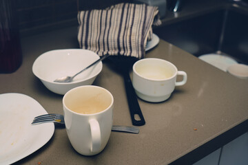 Many different dirty cups and plates on kitchen table near washbasin. Household concept.