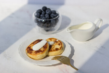 Cheese pancakes with blueberries on a white table. Morning rays of the sun. Good morning postcard