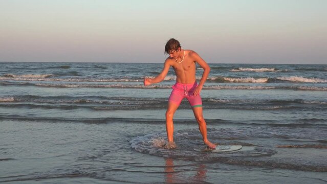 Handheld shot of teenager skim boarding along the beach at sunset