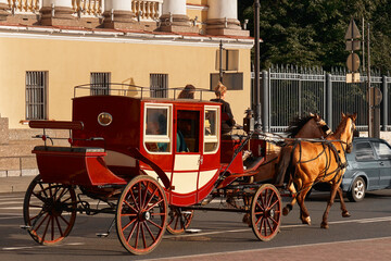 A red carriage drawn by two horses rides along a city road. Tourist excursion on retro transport.