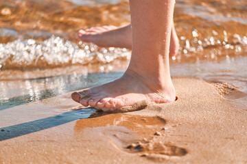 Children's feet stand on the sand of the sea beach and are washed by the waves, close-up. Girl...